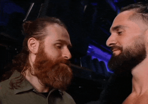 a man with a beard looks at another man with long hair