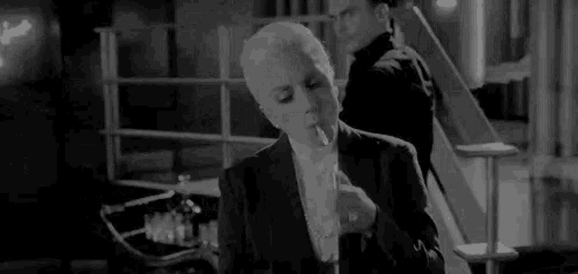 a woman is smoking a cigarette in a black and white photo while a man stands behind her .