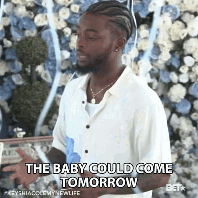 a man is standing in front of a wall of flowers and says the baby could come tomorrow