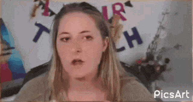 a woman is making a funny face in front of a sign that says ' picsart ' on it