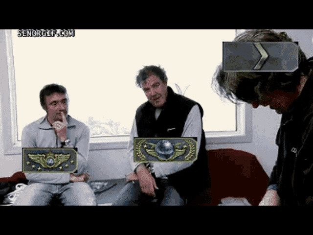 three men are sitting on a couch and one of them has a badge on his chest that says cg