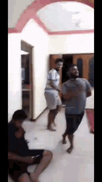 a group of men are dancing in a living room while a woman sits on the floor .