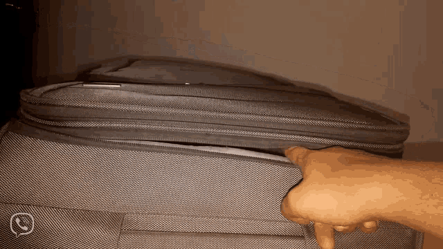 a person 's hand is reaching into a grey suitcase with a phone icon in the corner
