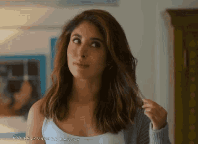 a woman in a white tank top and a grey sweater with the name karan kundra galaxy written on the bottom