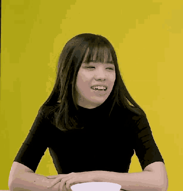 a young woman in a black shirt is sitting at a table with a bowl of food in front of her