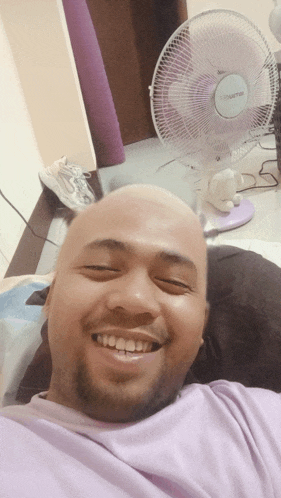 a man with a shaved head is smiling in front of a purple fan