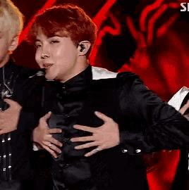 a man with red hair is holding his chest while wearing a black shirt and a microphone .