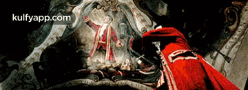 a man in a red cape is standing in front of a painting with the website kulfyapp.com in the corner