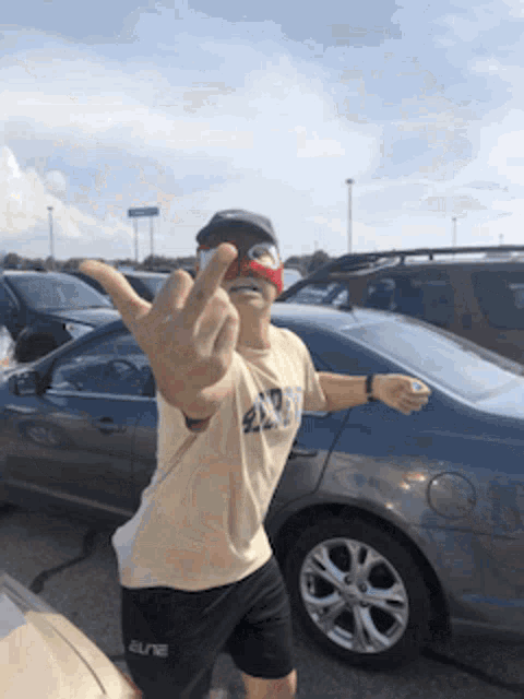a man giving the middle finger in front of a car that says elite