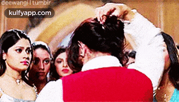 a man in a red vest is putting a bun on a woman 's hair .
