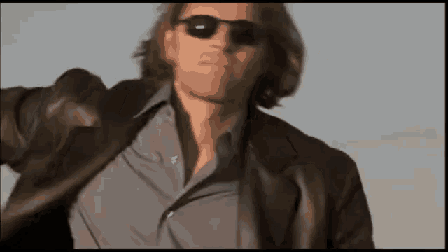 a man wearing sunglasses and a leather jacket is standing in the desert