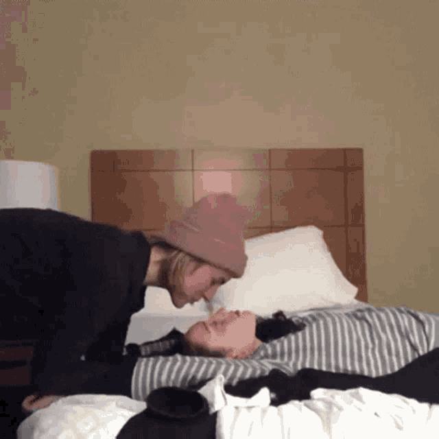 two women are kissing on a bed with one wearing a pink hat