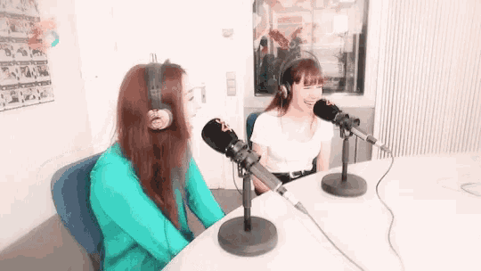 two women wearing headphones are sitting at a table in front of microphones .