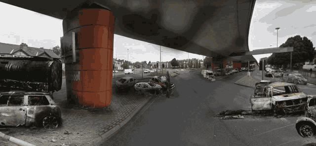 a row of burned cars sit under a bridge