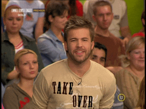 a man in a take over shirt stands in a crowd of people
