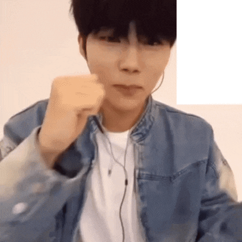 a young man wearing a denim jacket and earphones is making a fist .