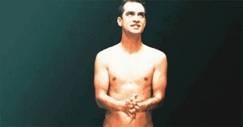 a naked man is standing in a dark room with his hands folded .