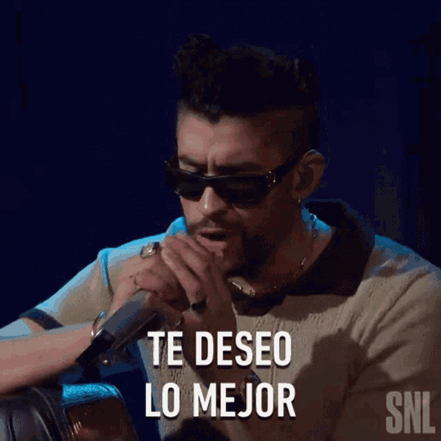 a man wearing sunglasses is singing into a microphone with the words te deseo lo mejor written below him