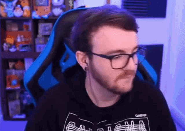 a man with a beard and glasses is sitting in a blue gaming chair .