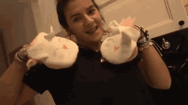 a woman in a black shirt is holding a pair of white slippers