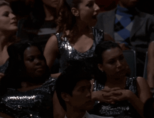 a group of people are sitting in a dark room and one of them is wearing a sequined top