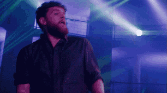 a man with a beard is dancing in a dark room with blue lights