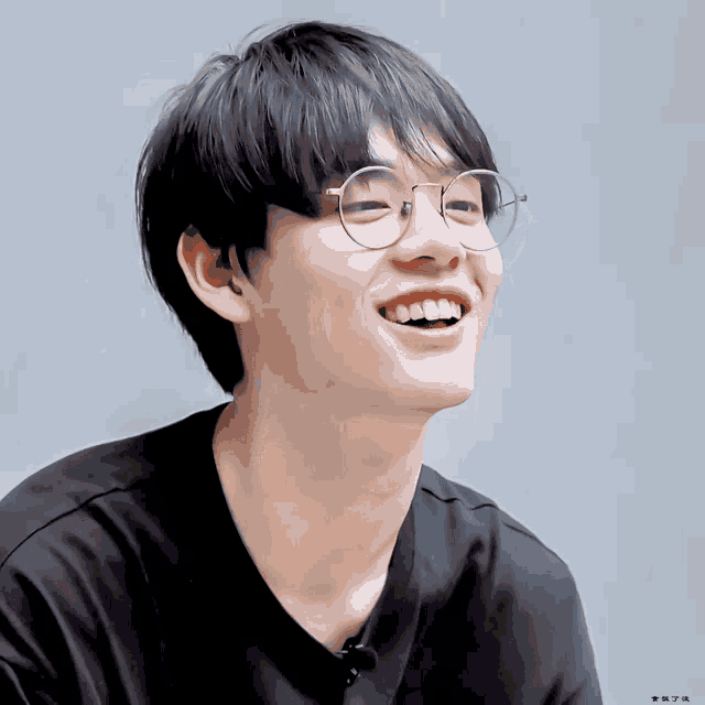 a young man wearing glasses and a black shirt smiles for the camera with a gray background