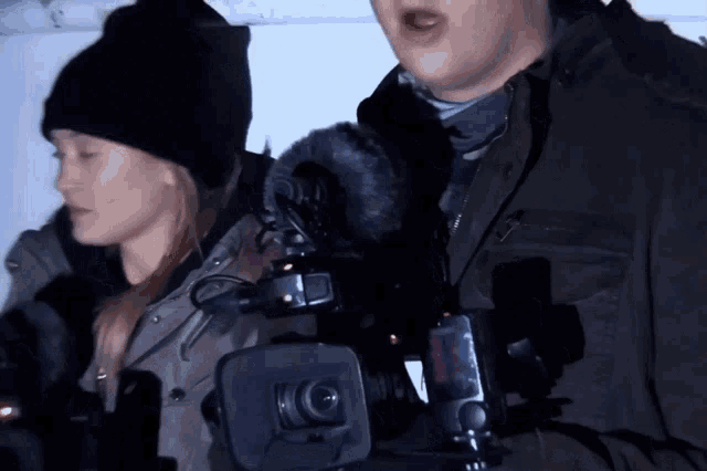 a man and a woman are standing next to each other holding a camera with a microphone attached to it
