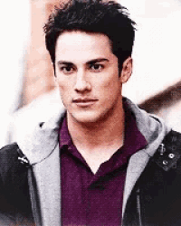 a man wearing a purple shirt and a grey jacket looks at the camera