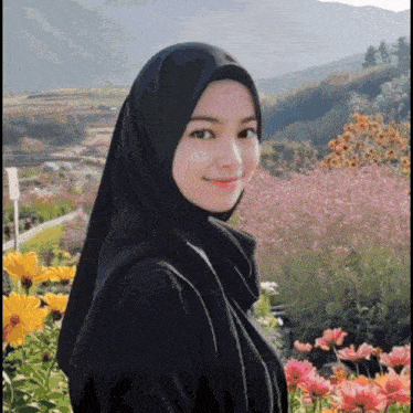 a woman wearing a black hijab stands in front of a field of flowers .