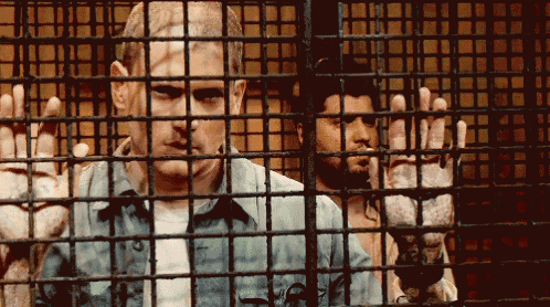 a man in a jail cell behind bars with his hands up