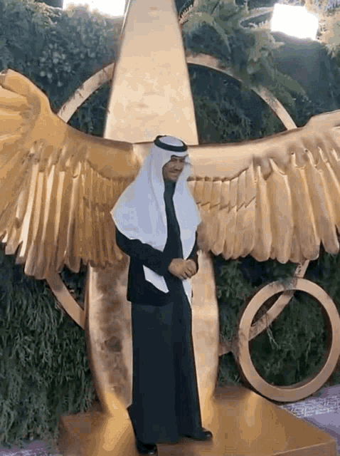a man in a turban stands in front of a large gold winged object