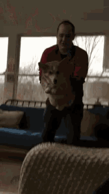 a man in a red shirt is holding a small dog in his arms