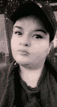 a woman with a piercing in her lip is wearing a baseball cap and a sweater .