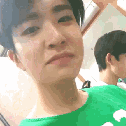 a man in a green shirt is taking a selfie with another man in the background .