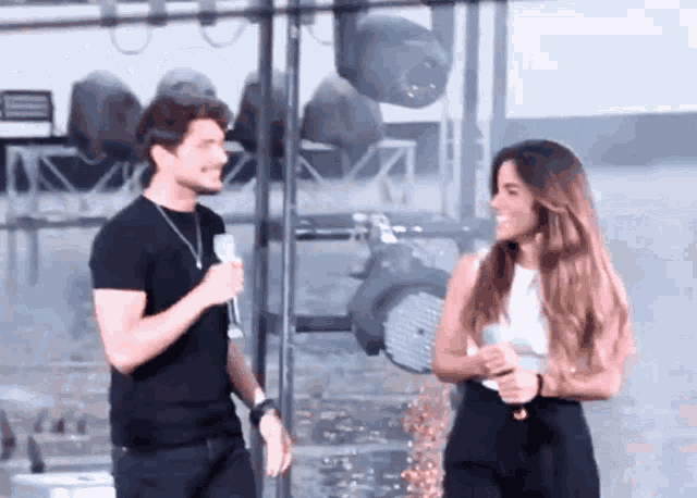 a man in a black shirt is talking to a woman in a white tank top