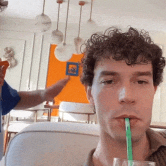 a man is drinking through a green straw from a glass