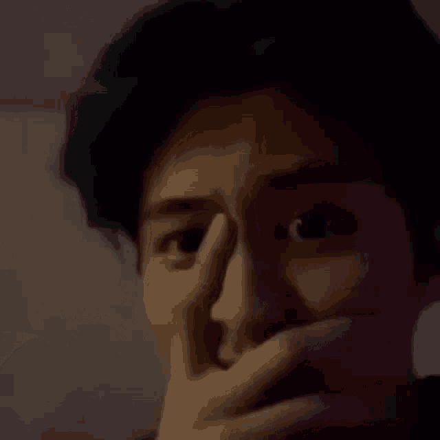 a man covering his mouth with his hand in a dark room