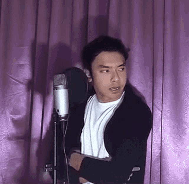a man is standing in front of a microphone with a purple curtain behind him