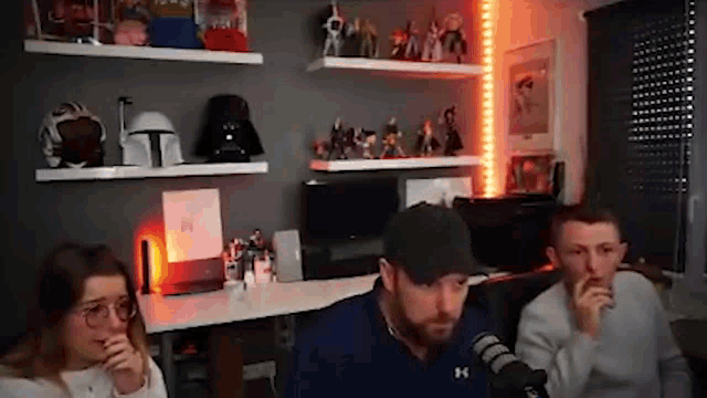 a group of people are sitting in front of a microphone in a room with shelves filled with toys .