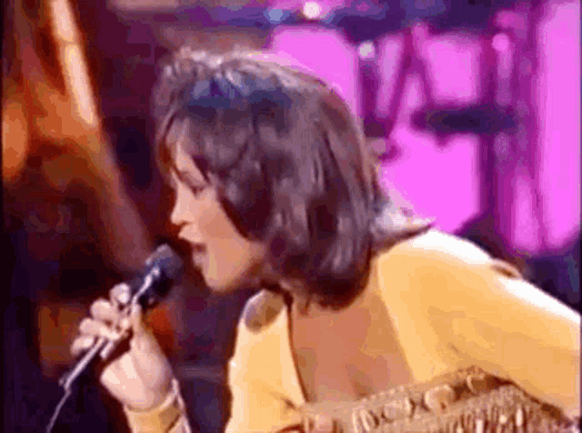 a woman is singing into a microphone on stage in front of a pink background .