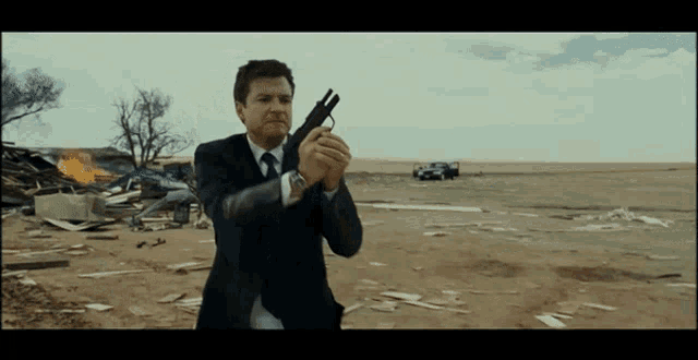 a man in a suit holds a gun in a field