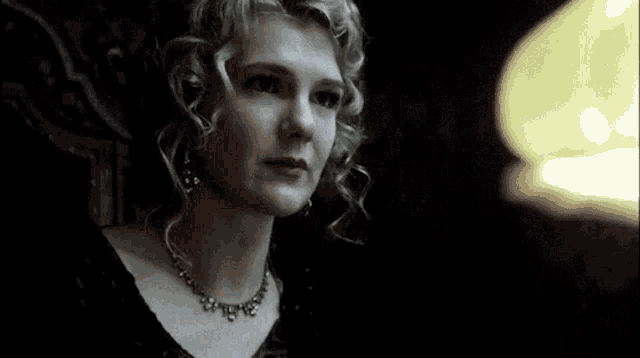 a woman with curly hair wearing a necklace looks up