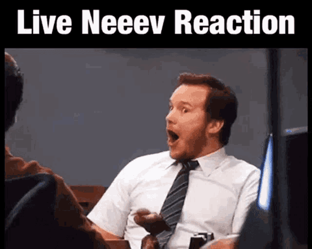 a man in a suit and tie is sitting in a chair with his mouth open and the words live neeev reaction written above him .