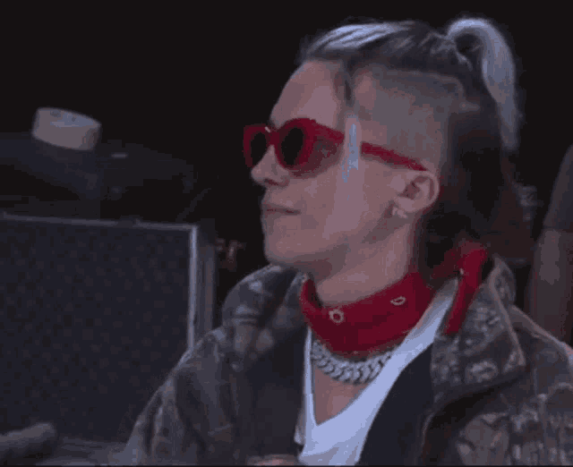 a man wearing sunglasses and a red bandana looks at the camera