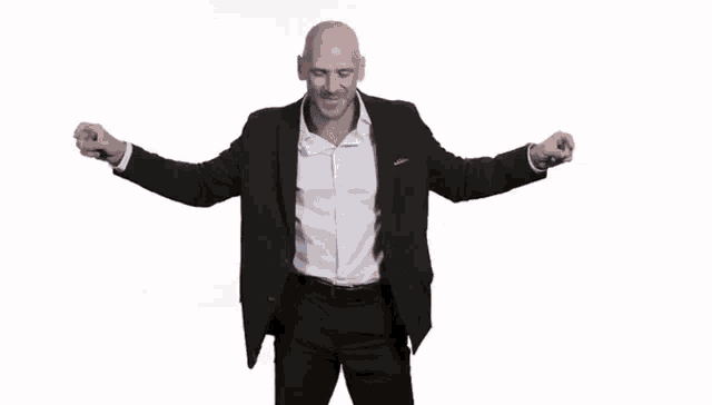 a bald man in a black suit and white shirt is dancing with his arms outstretched