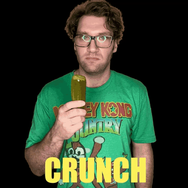 a man wearing a green shirt that says donkey kong country holds a pickle