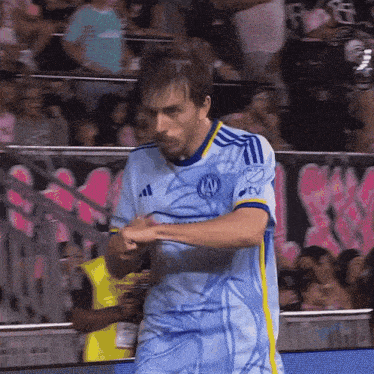 a man in a blue and yellow adidas jersey stands in front of a stadium full of people