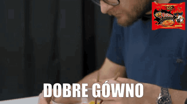 a man is eating noodles with a package of noodles behind him that says dobry gowno