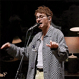 a man wearing glasses is singing into a microphone while wearing a checkered shirt .